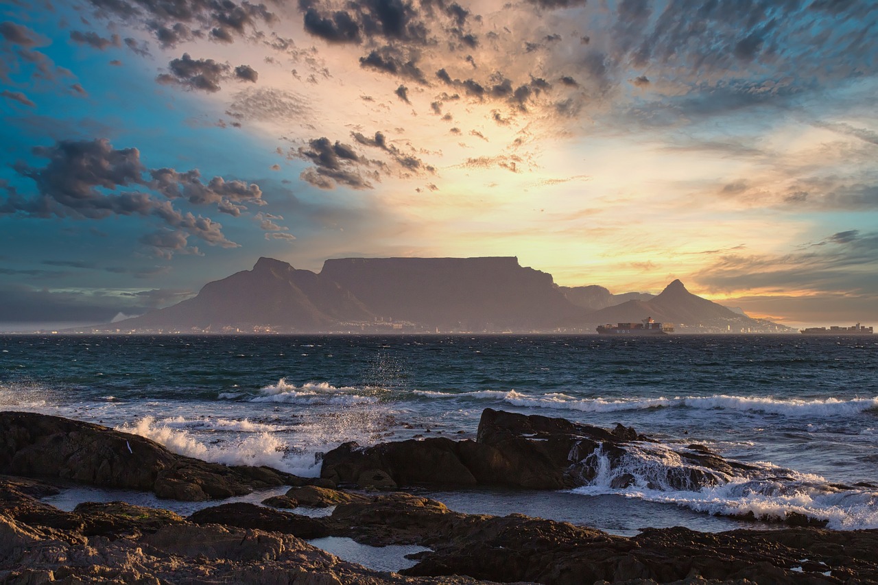 A picture of a mountain with the beach infront of it and clouds above the mountain